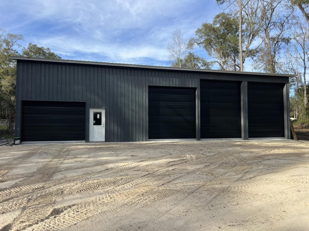 Completed steel pole barn with dark metal siding and three garage doors